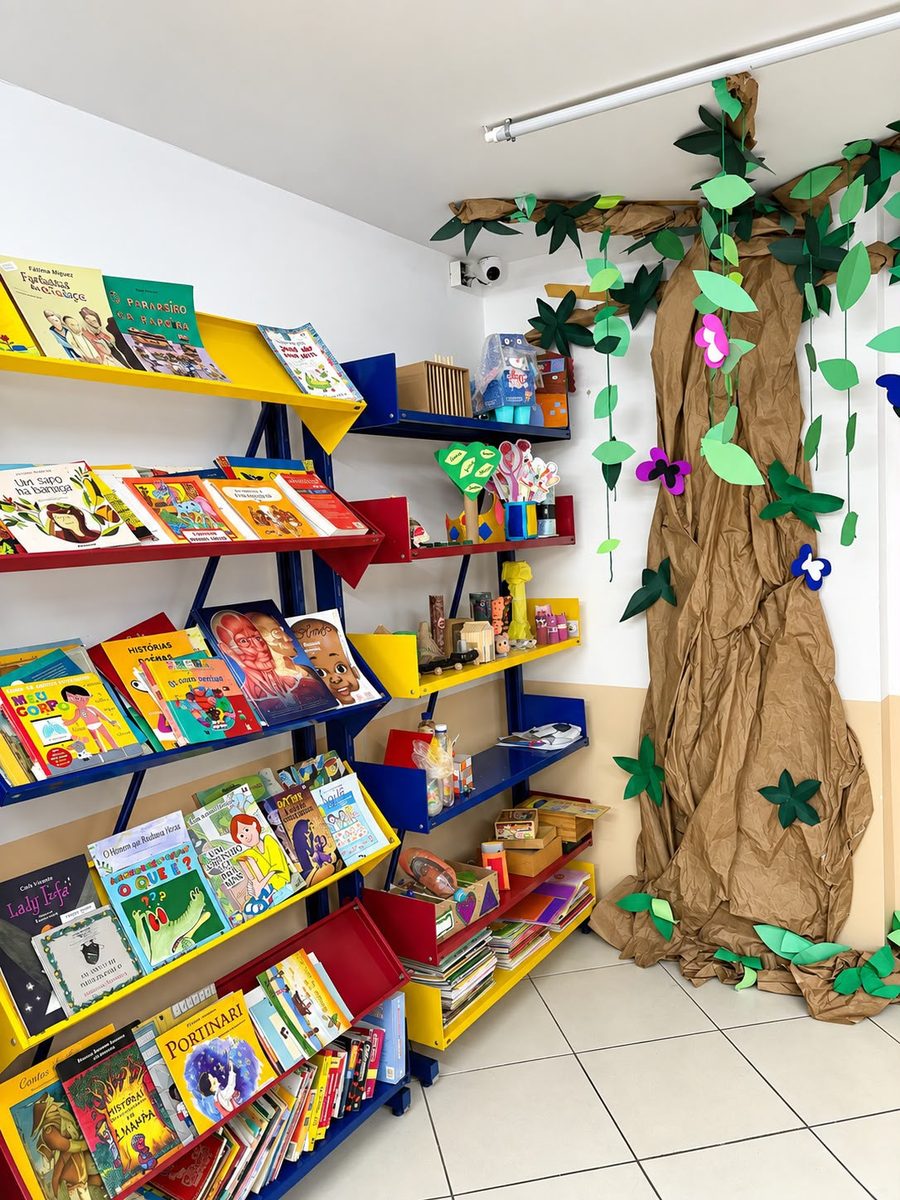 Biblioteca da escola com estantes coloridas de livros infantis e árvore decorativa