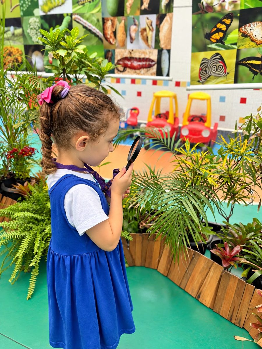 Criança observando as plantas com uma lupa no jardim da escola